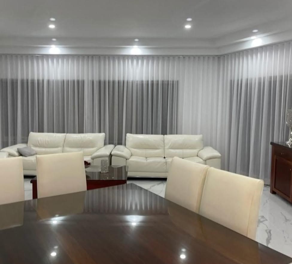 Grey sheer curtains behind a white leather lounge suite