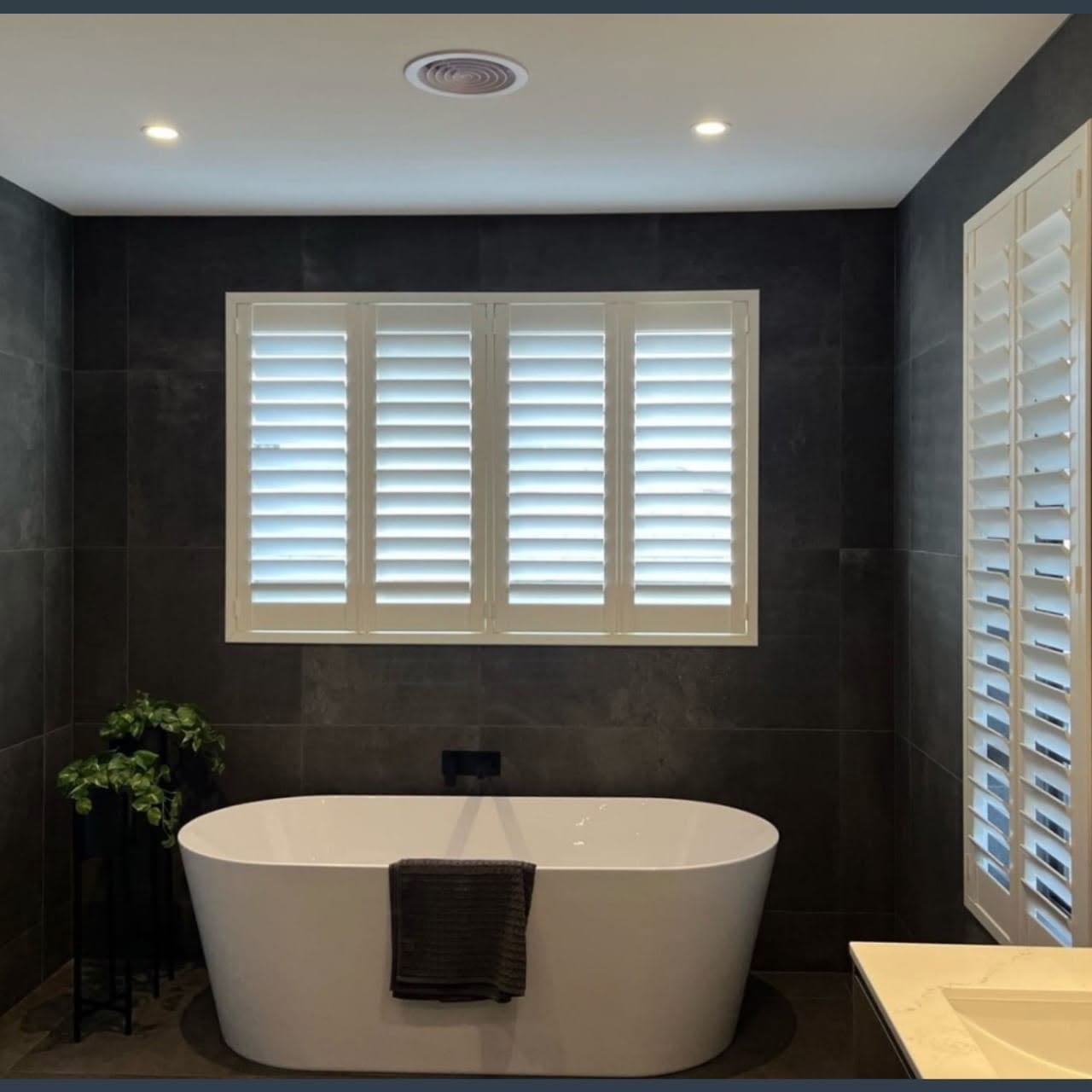 White plantation shutters in a charcoal-tiled bathroom