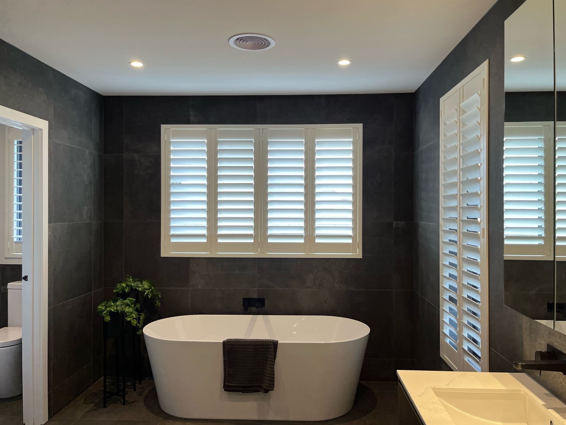 Plantation shutters in a dark-tiled ensuite